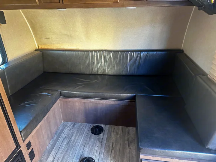 U-shaped dinette seating with black cushions and wood accents in an RV rental interior, showing floor bases for a table.. Sunset Park RV Sun Lite 2020