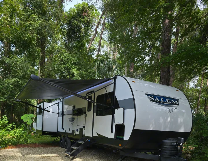 Experience nature with this Salem Platinum RV rental parked amidst lush trees, featuring an extended awning for shade.. Forest River Salem Platinum 2024
