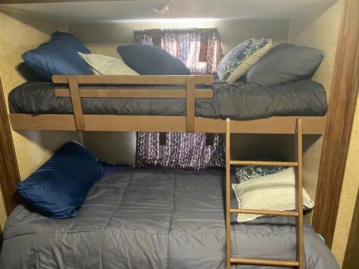 Inside this RV rental, two bunk beds are neatly made with dark bedding and assorted pillows, featuring a wooden ladder for access.. KZ Sportsman 2015