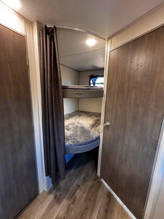 Cozy RV rental interior featuring comfortable bunk beds with grey bedding, a privacy curtain, and wood-look flooring.. Coachmen Catalina Summit Series 8 261BHS 2025