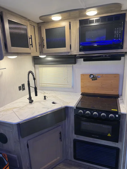 Modern RV rental kitchen featuring microwave, stove, sink, and light-toned cabinets and counters.. Forest River Cherokee Alpha Wolf 2022