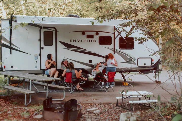 Group of women socializing outside a large rv rental, enjoying a relaxing time at their woodland campsite.. Gulf Stream Envision 2020