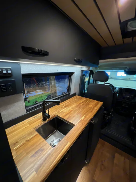 Spacious RV rental interior with a modern kitchenette, wood counters, and sink. Perfect for your next adventure.. Dodge Ram Promaster 2025