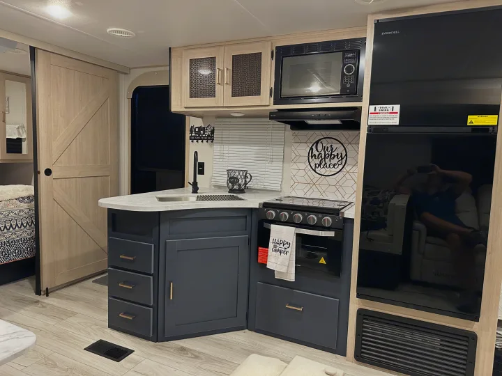 Modern RV rental interior: compact kitchen with full-size fridge, stove, sink, and barn door to bedroom.. Prime Time Avenger 27DBS 2024