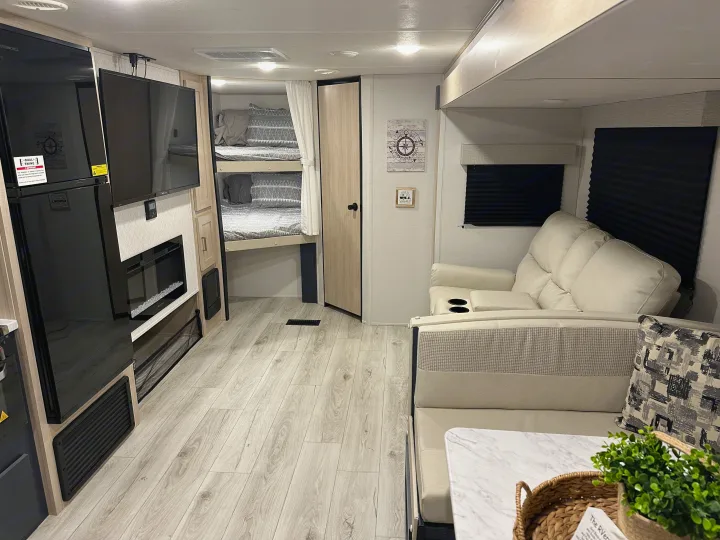 Spacious RV rental interior featuring a large fridge, TV, fireplace, bunk beds, and comfortable dinette and couch seating.. Prime Time Avenger 27DBS 2024