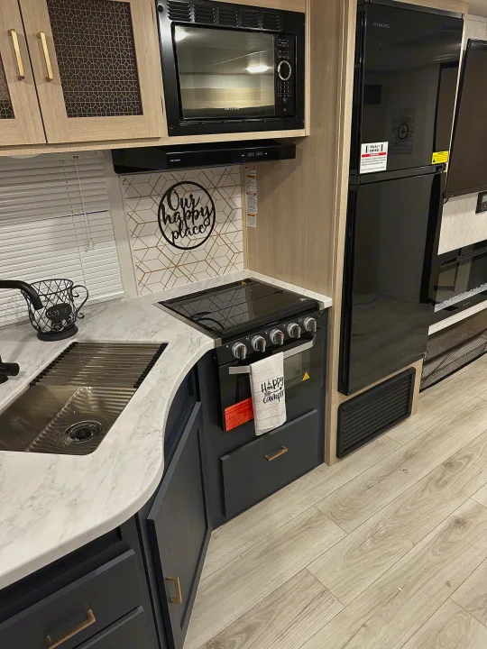 A modern RV rental kitchen featuring a sink, stove, microwave, and tall refrigerator.. Prime Time Avenger 27DBS 2024