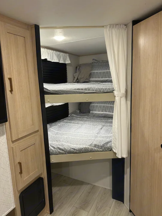 RV rental interior: Two stacked bunk beds with geometric grey bedding & white privacy curtains.. Prime Time Avenger 27DBS 2024