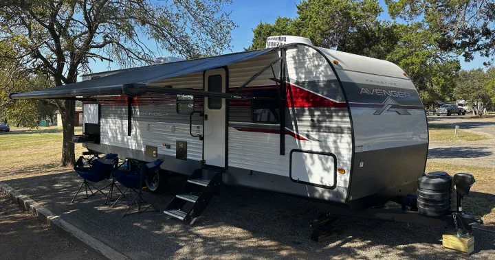 This **RV rental**, a Primetime Avenger travel trailer, is parked at a sunny campsite with its awning extended for leisure.. Prime Time Avenger 27DBS 2024