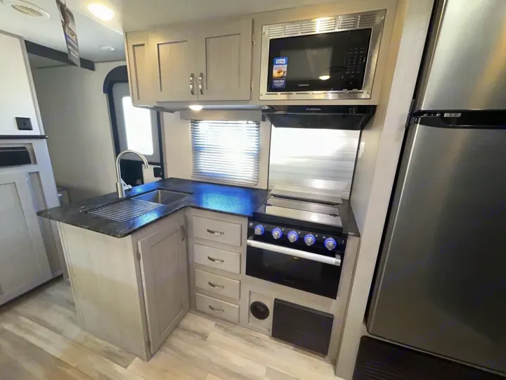Compact RV rental kitchen with light cabinetry, dark counters, stainless steel sink, oven, microwave, and fridge.. Forest River Tracer 2022