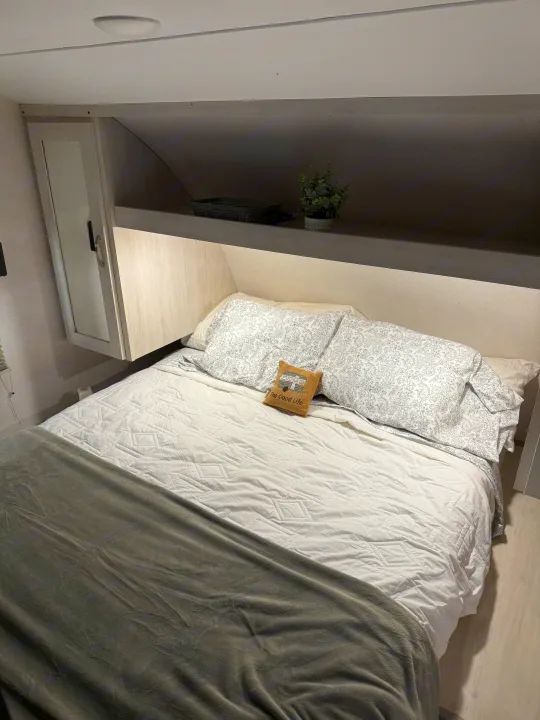Cozy RV rental bedroom featuring a comfortable bed with patterned pillows, overhead storage, and a mirrored cabinet.. Forest River Tracer 2022