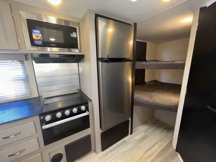 RV rental interior features a compact kitchen with modern appliances, alongside two comfy bunk beds for travelers.. Forest River Tracer 2022