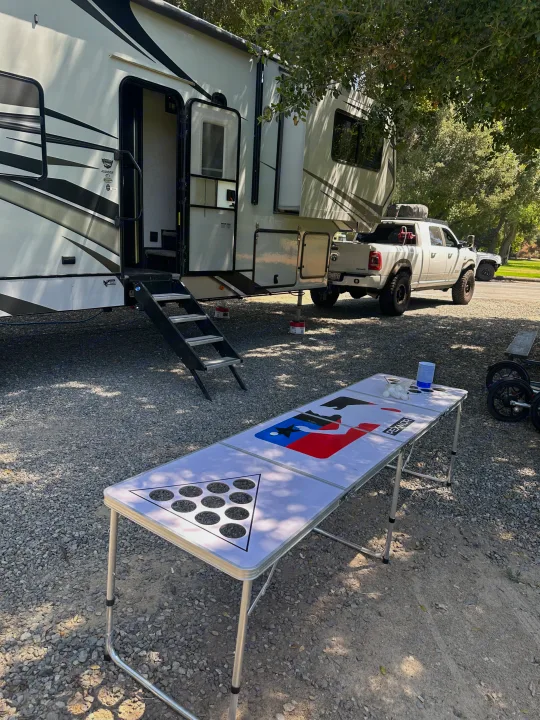 Enjoying an RV rental adventure! A large white RV and pickup truck at a gravel campsite, with a beer pong table set up.. Eclipse Recreational Vehicles Attitude 2020