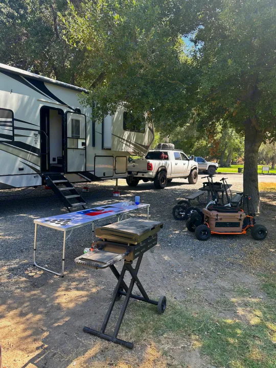 Sunny RV rental campsite with a large fifth-wheel, pickup truck, grill, beer pong table, and electric carts under tall trees.. Eclipse Recreational Vehicles Attitude 2020