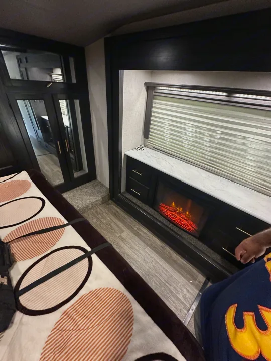 Modern RV rental interior: a cozy bedroom setup with a stylish blanket, reflective doors, and a warm electric fireplace.. Eclipse Recreational Vehicles Attitude 2020