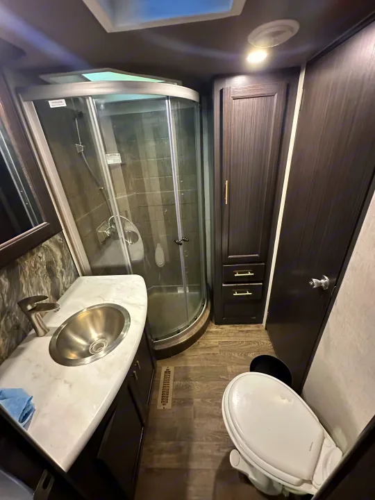 Inside an RV rental, this modern bathroom features a curved glass shower, vanity with stainless sink, toilet, and dark wood finishes.. Eclipse Recreational Vehicles Attitude 2020