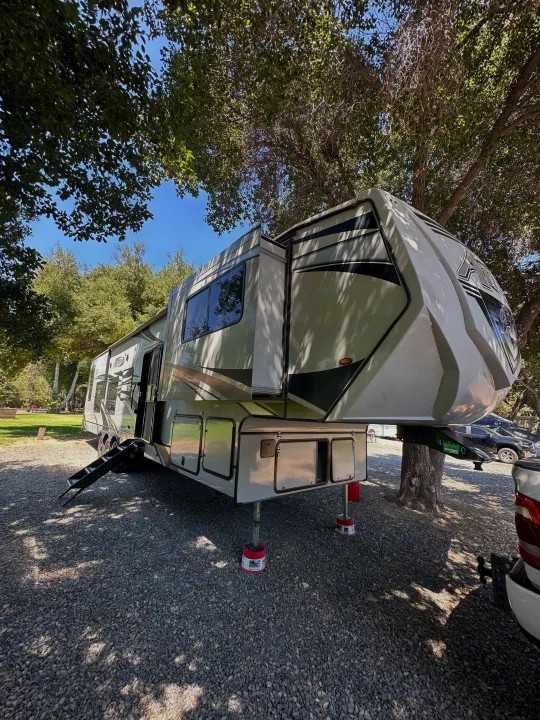 Enjoy the outdoors with this large fifth-wheel RV, perfect for an rv rental, parked on gravel under shady trees at a sunny campsite.. Eclipse Recreational Vehicles Attitude 2020