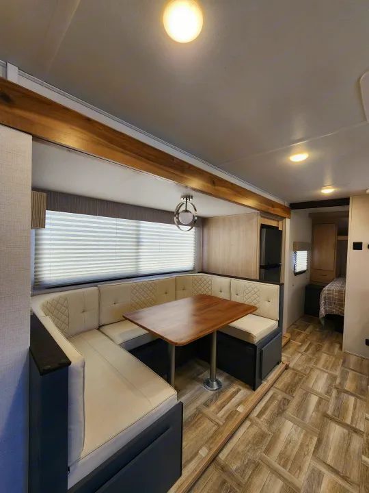 Bright RV rental interior: a U-shaped dinette with wood table, adjacent refrigerator, and bedroom view. Modern and functional.. primetime tracer 2024