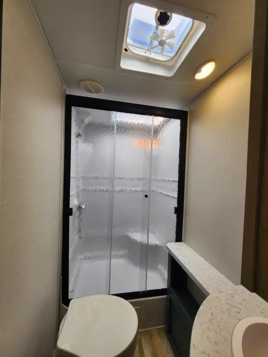 Spacious RV rental bathroom with a textured glass shower, toilet, vanity, and ceiling fan.. primetime tracer 2024