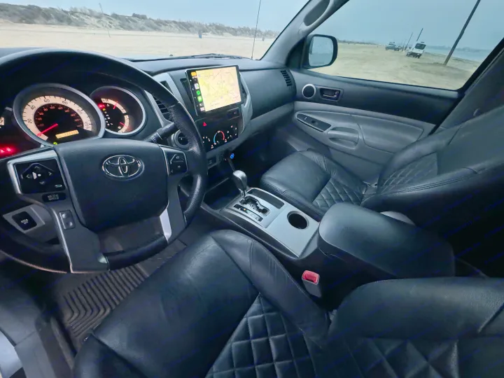 Interior of a truck with a navigation map, odometer at 113,999 miles. Outside, an RV rental and other vehicles are on a sandy beach.. Adventurer 2015 Tacoma 2024