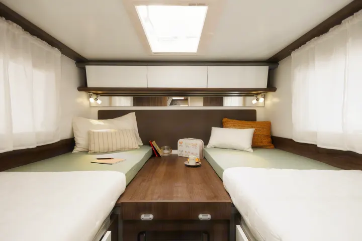 Bright RV rental bedroom features two single beds, central wooden console, overhead storage, and a skylight.. Benimar Tessoro 463UP 2025