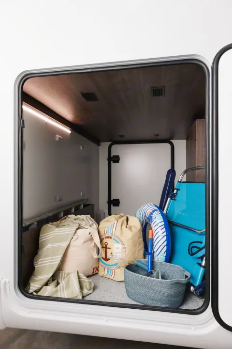 Inside an RV rental's spacious storage bay, well-lit and organized with beach gear, bags, and a folded chair.. Benimar Tessoro 463UP 2025
