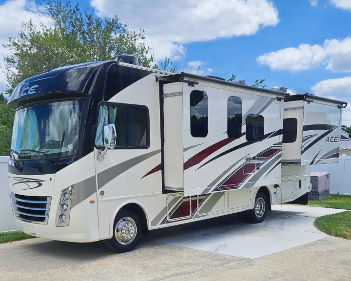 A large, clean white and black motorhome with extended slide-out parked on concrete, seen in daylight, ideal for rv rental.. Thor A.C.E. 2020