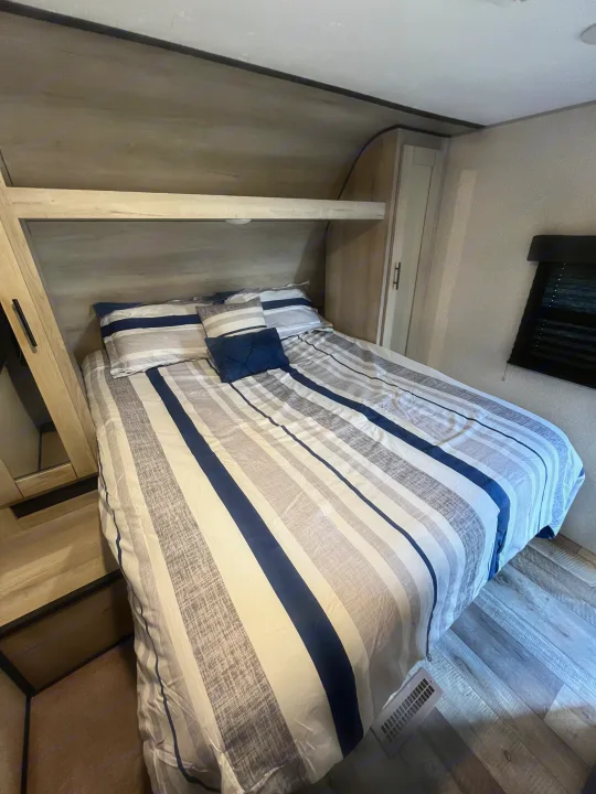 Cozy RV rental bedroom with a large bed, blue and grey striped bedding, built-in storage, and light wood-look floor.. KZ Connect 2021