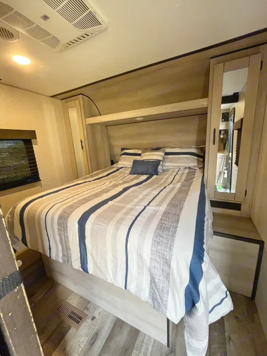 Cozy RV rental bedroom with striped bedding, overhead storage, and a ceiling AC unit.. KZ Connect 2021