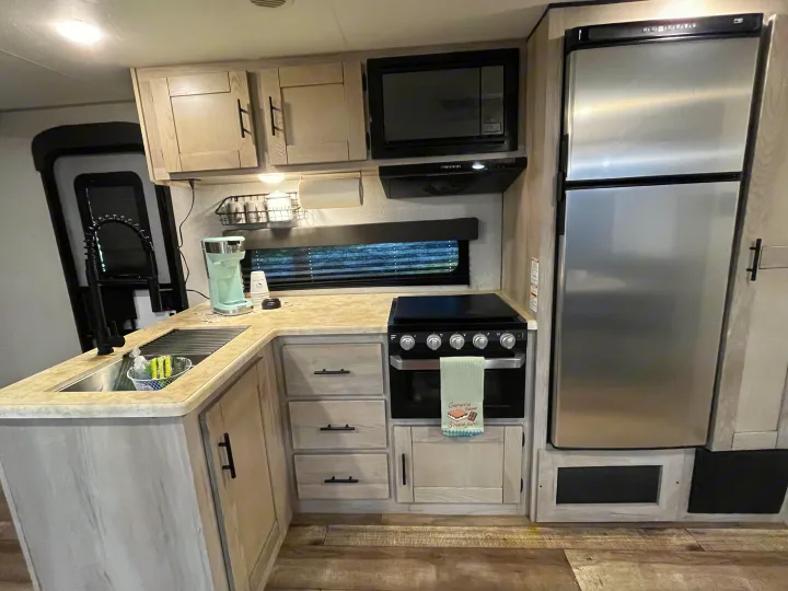 Modern RV rental kitchen featuring a sink, microwave, oven, and refrigerator. Light wood cabinets complete the functional space.. KZ Connect 2021