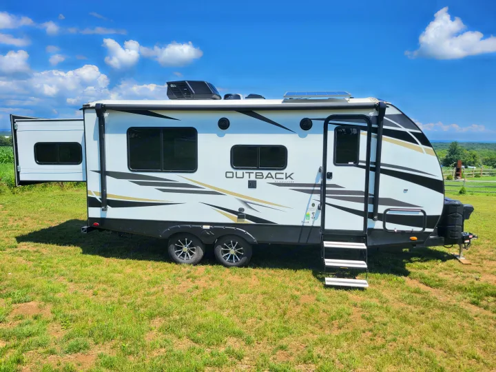 White Outback by Keystone **RV rental** with open slide-out & steps, parked on grass under a clear sky. Ready for travel!. Keystone RV Outback Ultra-Lite 2022