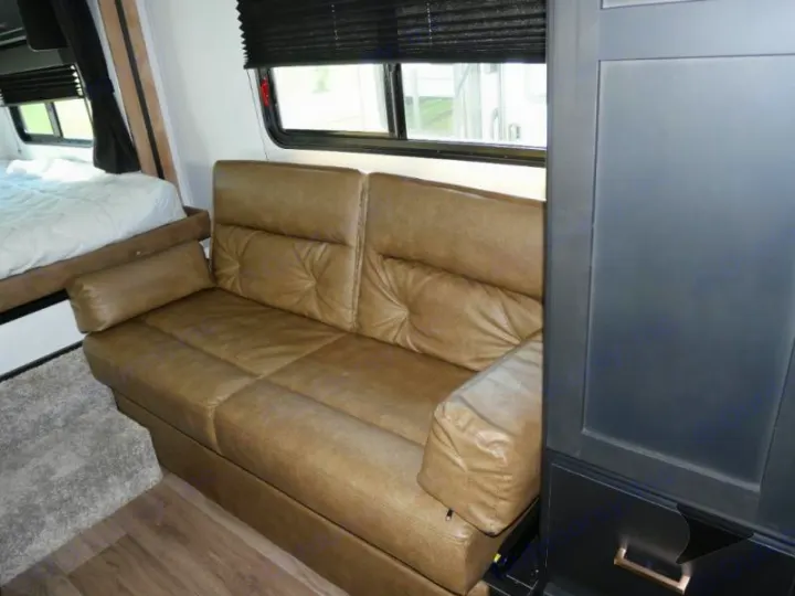 Spacious RV rental interior featuring a comfy tan sofa, a bed with white linens, and a dark storage cabinet.. Keystone RV Outback Ultra-Lite 2022