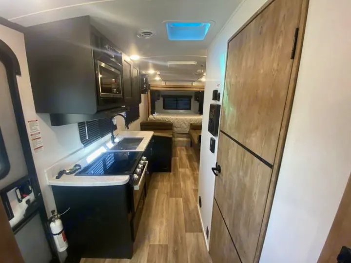 View of an RV rental's interior, showing a galley kitchen with counter space, sink, stove, and a bed in the rear.. Keystone RV Outback Ultra-Lite 2022