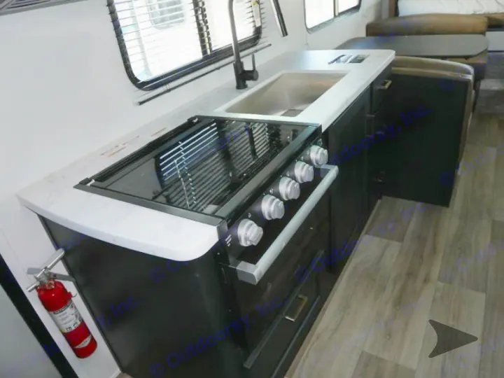 Inside an RV rental, featuring a sleek kitchen with white marbled countertop, black stove, sink, and an accessible fire extinguisher.. Keystone RV Outback Ultra-Lite 2022