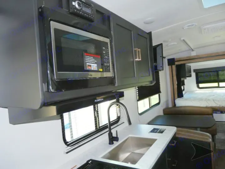 Inside an RV rental: a compact kitchen with microwave, sink, and countertop, flowing into a dinette and cozy bedroom.. Keystone RV Outback Ultra-Lite 2022