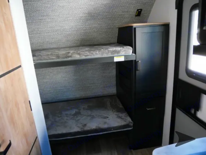 RV rental's cozy interior features bunk beds with grey mattresses and a black storage cabinet. Compact and functional.. Keystone RV Outback Ultra-Lite 2022