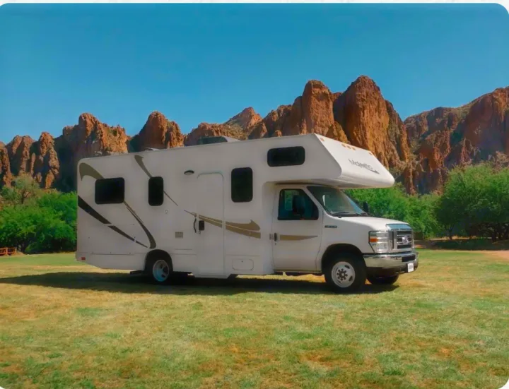Majestic RV rental on a grassy field against a backdrop of rugged mountains and blue sky, perfect for adventures.. Thor Majestic 2019
