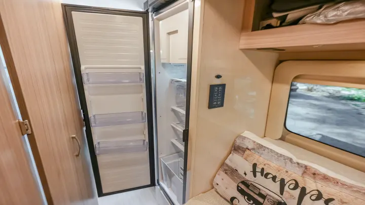 An open refrigerator and built-in amenities in a modern RV rental interior, with a window view outside.. Jayco swift 2024