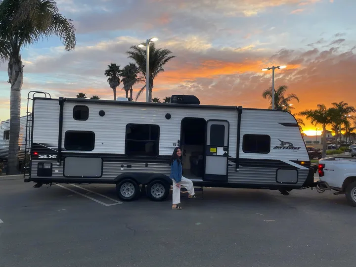 Stunning sunset over a new Jay Flight RV rental. Woman smiles on its steps, ready for travel & adventure.. Jayco Jay Flight SLX 2022