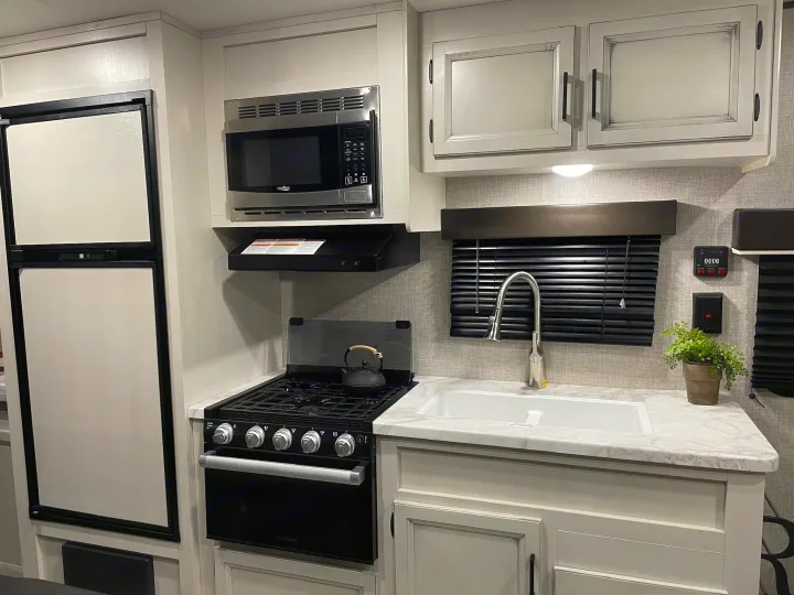 Modern RV rental kitchen with a refrigerator, microwave, stove, and sink. Clean, functional cooking space.. Jayco Jay Flight SLX 2022