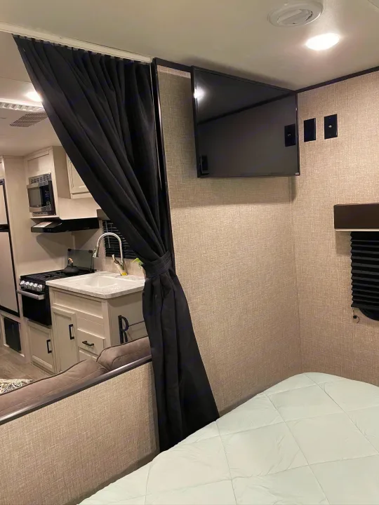 Explore this cozy RV rental interior, showcasing a compact kitchen, private curtain, mounted TV, and comfortable sleeping area.. Jayco Jay Flight SLX 2022