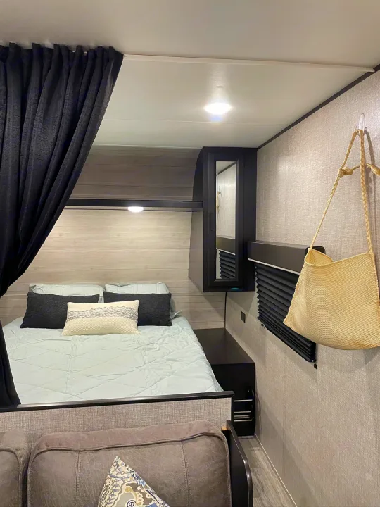 RV rental interior: cozy bedroom with a bed, dark curtain, cabinet, and a straw bag on a textured wall.. Jayco Jay Flight SLX 2022