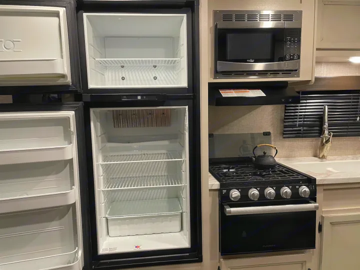 Empty RV rental kitchen: open fridge, freezer, microwave, and gas stove/oven with a kettle. Perfect for your next trip.. Jayco Jay Flight SLX 2022