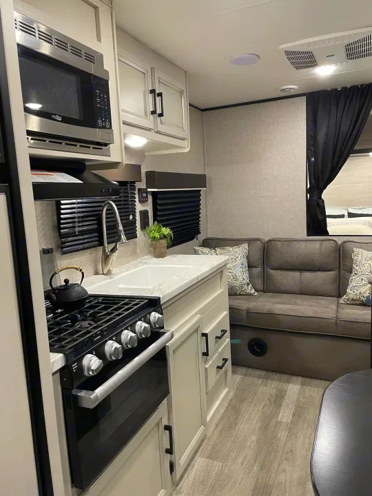 Inside a modern RV rental: a compact kitchen with microwave, stove, oven, and sink, beside a cozy sofa.. Jayco Jay Flight SLX 2022