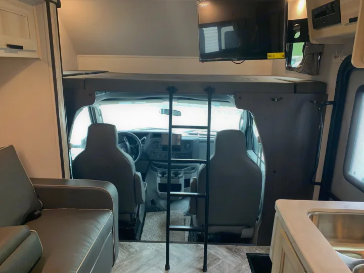 Cozy RV rental interior: view of cab, bunk bed with ladder, TV, sofa, and kitchen counter.. Forest River Sunseeker 2027