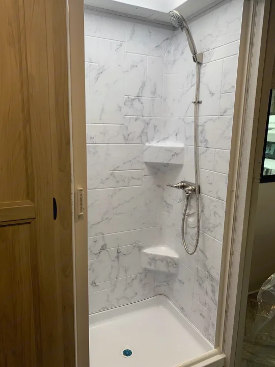 Modern RV rental shower with marble-look walls and handheld showerhead. Compact design for comfortable travels.. Forest River Sunseeker 2027