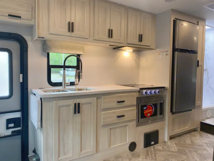RV rental interior kitchen with light wood cabinets, stainless steel appliances including fridge, microwave, stove, and sink.. Forest River Sunseeker 2027