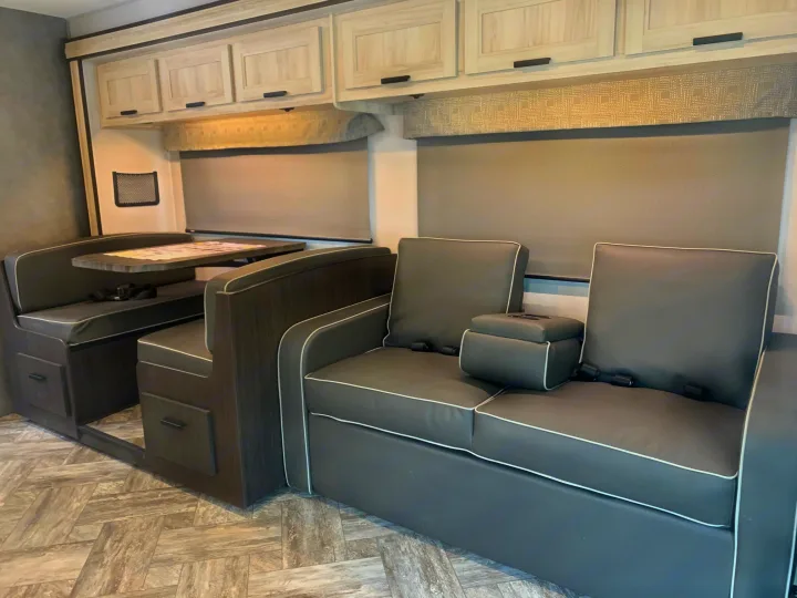Spacious RV rental interior with a dinette, comfy sofa with armrest console, and overhead cabinets for travel.. Forest River Sunseeker 2027