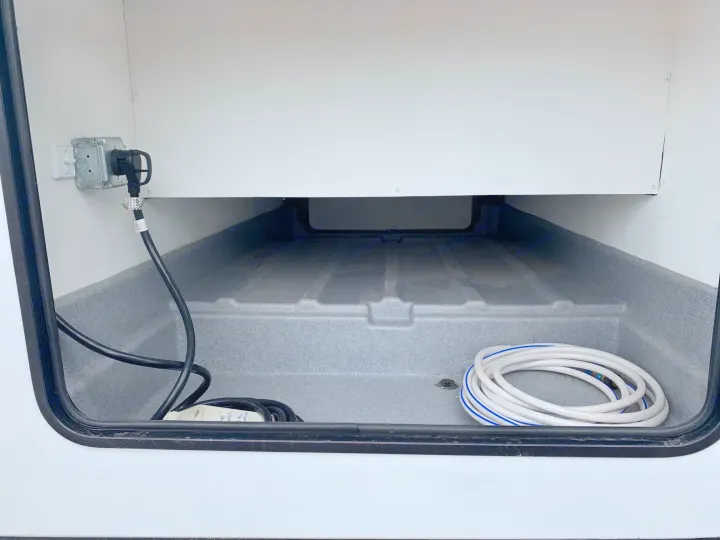 RV rental's clean storage bay: shore power plug, electrical cords, and coiled fresh water hose.. Forest River Sunseeker 2026