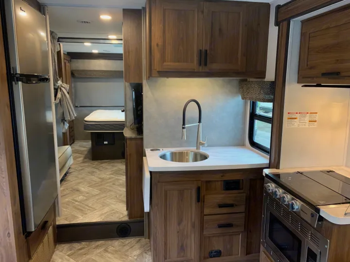 Step into this **RV rental**! A modern interior with a fully equipped kitchen (sink, stove, fridge) and a glimpse of the bedroom.. Forest River Sunseeker 2026