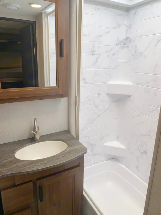 Modern RV rental bathroom with vanity, sink, and stylish marble-look shower/tub combo.. Forest River Sunseeker 2026